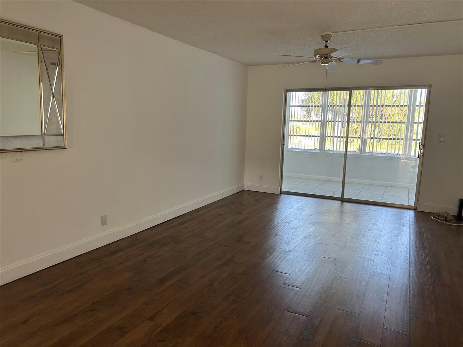 An empty living room features dark wood-look flooring, white walls, a ceiling fan, and sliding doors — 7807 Golf Circle Drive # 205, Margate FL 33063, MARGATE, FL