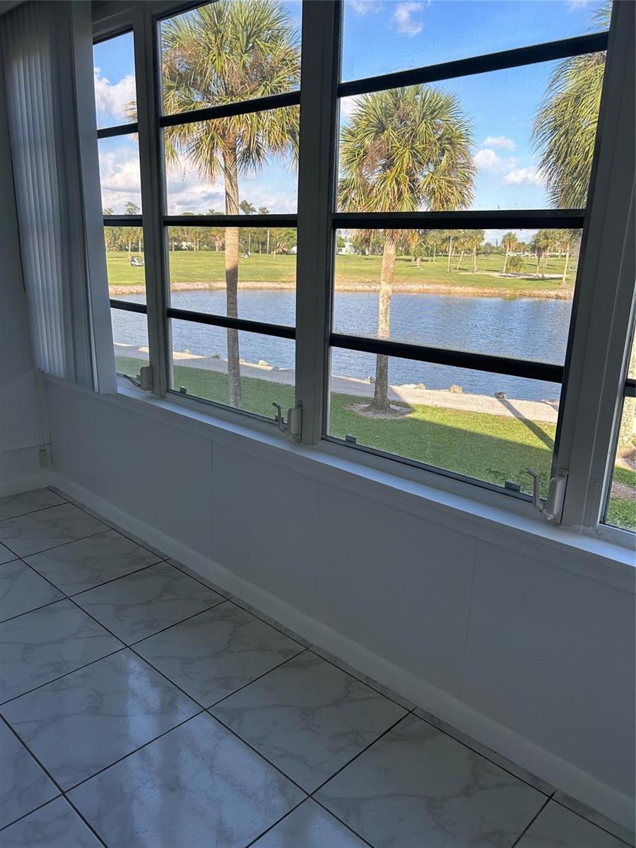A sunroom with white tile flooring features large windows overlooking a lake and golf course — 7807 Golf Circle Drive # 205, Margate FL 33063, MARGATE, FL