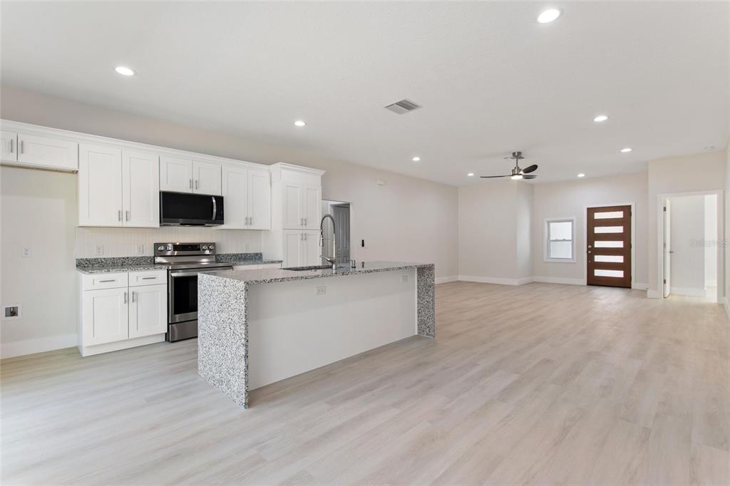 A kitchen with white cabinets, granite countertops, and an island opens to a living area — 3770 JAPONICA AVENUE, INDIAN LAKE ESTATES, FL