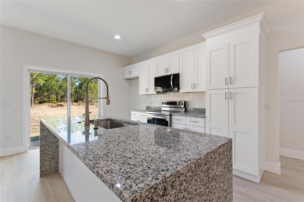 A kitchen features white cabinetry, granite countertops, a large island, and a sliding glass door — 3770 JAPONICA AVENUE, INDIAN LAKE ESTATES, FL