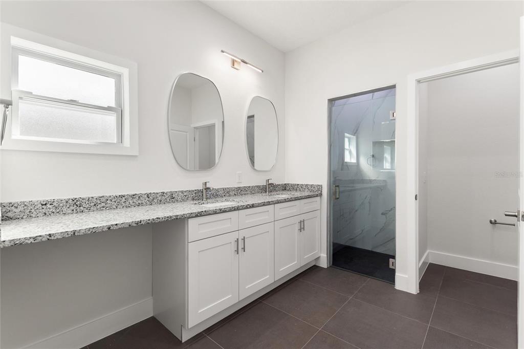 A bathroom features a double vanity with granite countertops, white cabinets, and a glass-enclosed shower — 3770 JAPONICA AVENUE, INDIAN LAKE ESTATES, FL