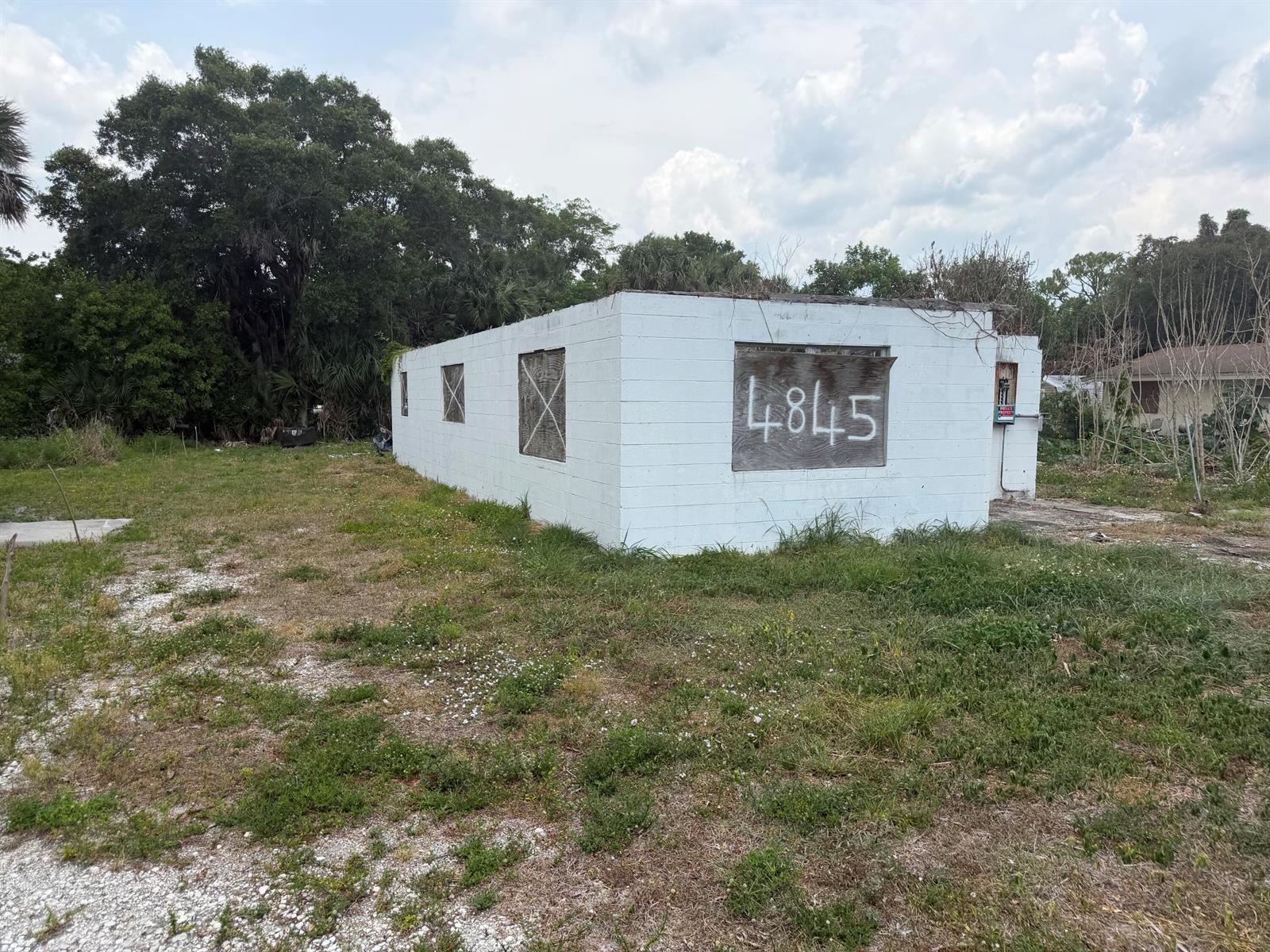 A small, white, concrete block building with boarded-up windows stands on a grassy lot — 4845 34th Avenue, Vero Beach FL 32967, VERO BEACH, FL