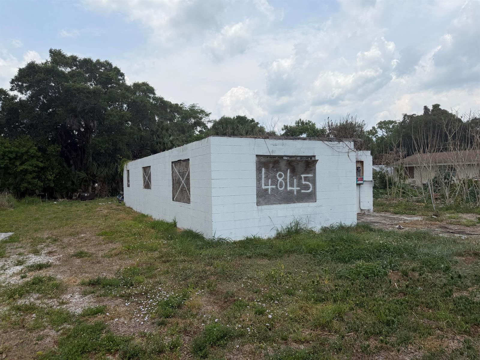 A small, white, concrete block building with boarded-up windows sits on a grassy lot — 4845 34th Avenue, Vero Beach FL 32967, VERO BEACH, FL