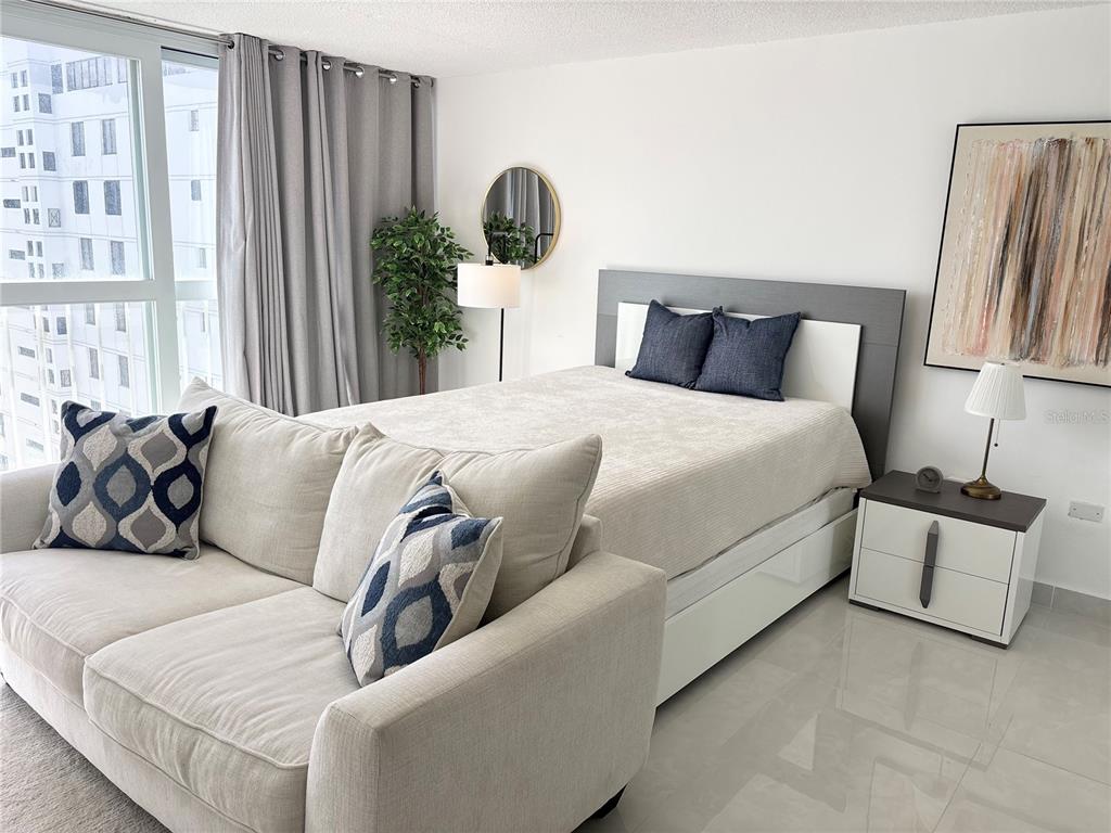 A bedroom features a bed, a sofa, a nightstand, and a large window with curtains — 1035 ASHFORD AVENUE UNIT 1108, SAN JUAN, PR
