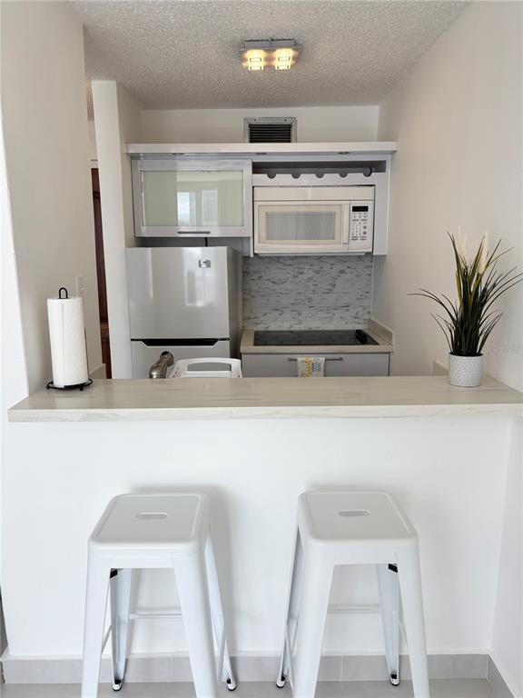 A small kitchen features white cabinets, a microwave, a refrigerator, and a breakfast bar — 1035 ASHFORD AVENUE UNIT 1108, SAN JUAN, PR