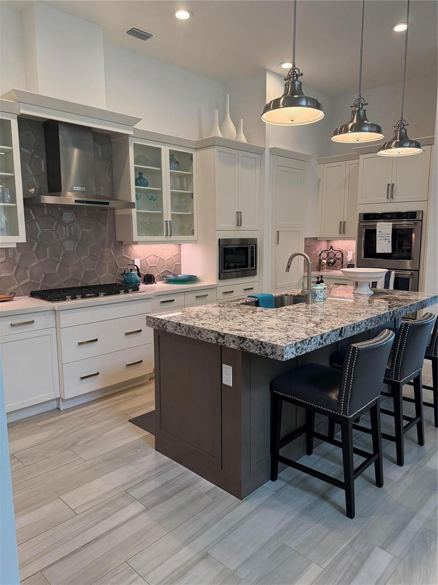 A modern kitchen features white cabinetry, a dark island with granite countertops, and gray tile flooring — 8467 Grand Prix Lane, Boynton Beach FL 33472, BOYNTON BEACH, FL