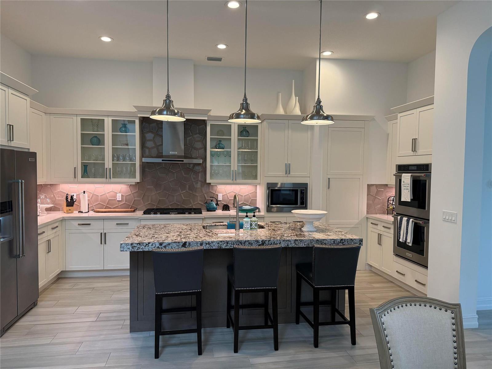 A modern kitchen features white cabinets, a granite-topped island, stainless steel appliances, and tile backsplash — 8467 Grand Prix Lane, Boynton Beach FL 33472, BOYNTON BEACH, FL