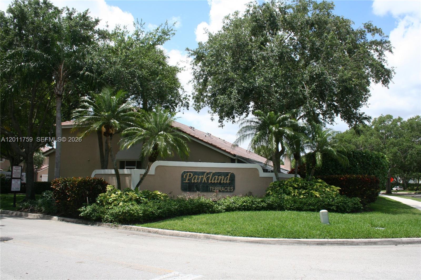 A beige stucco sign for Parkland Terraces stands in a landscaped area with palm trees — 6200 NW 74th Ct, Parkland FL 33067, PARKLAND, FL