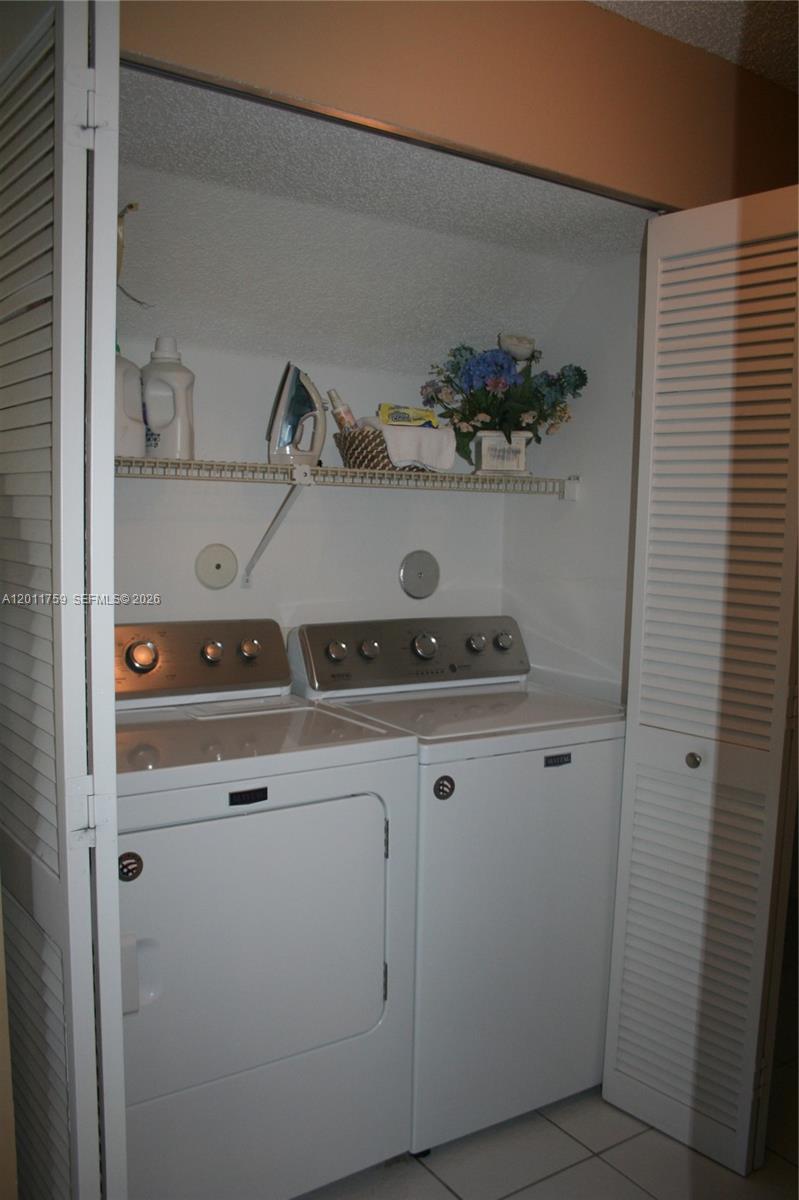 A laundry closet features a white washer and dryer with a wire storage shelf above — 6200 NW 74th Ct, Parkland FL 33067, PARKLAND, FL