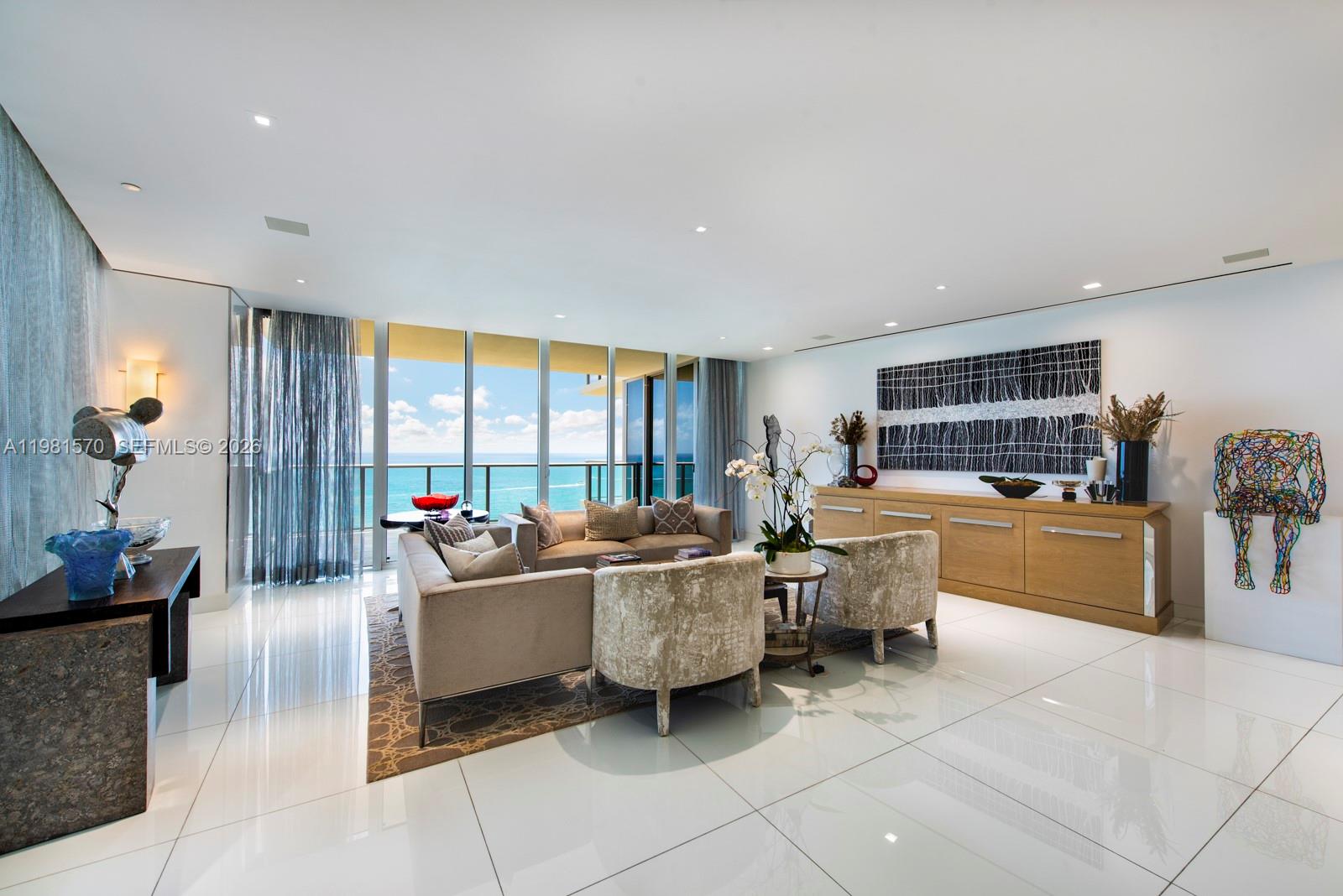 A modern living room features white tile floors, neutral furniture, and floor-to-ceiling windows overlooking the ocean — 9705 Collins Ave # 1702N, Bal Harbour FL 33154, BAL HARBOUR, FL
