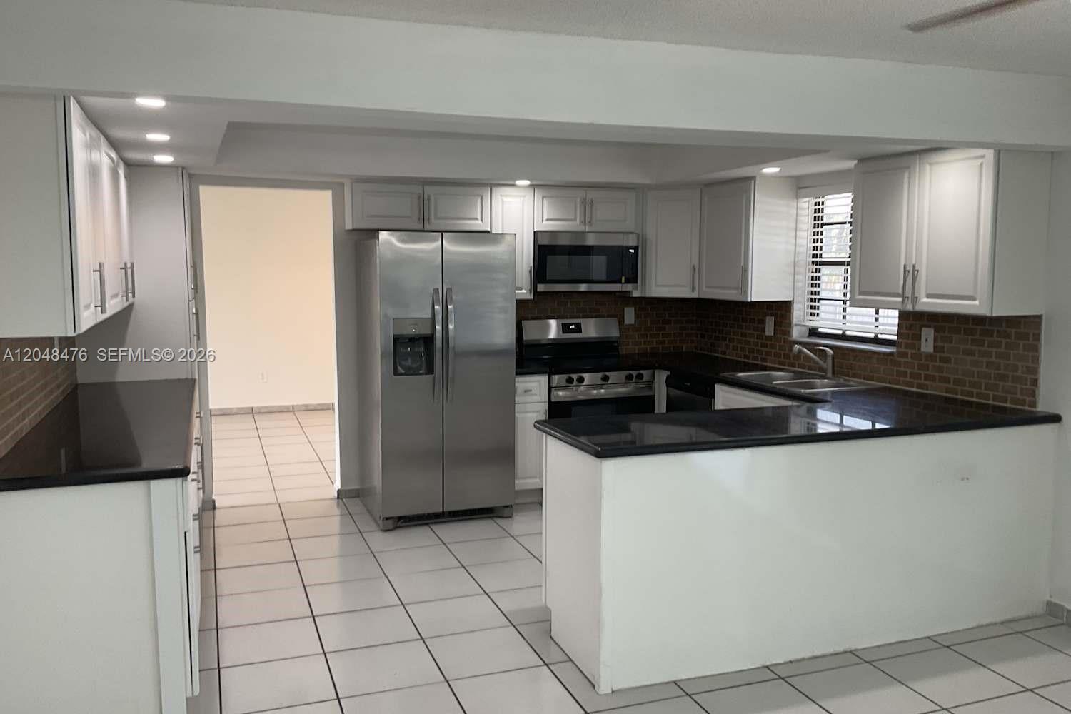 A kitchen features white cabinets, stainless steel appliances, black countertops, and light-colored tile flooring — CUTLER BAY, FL