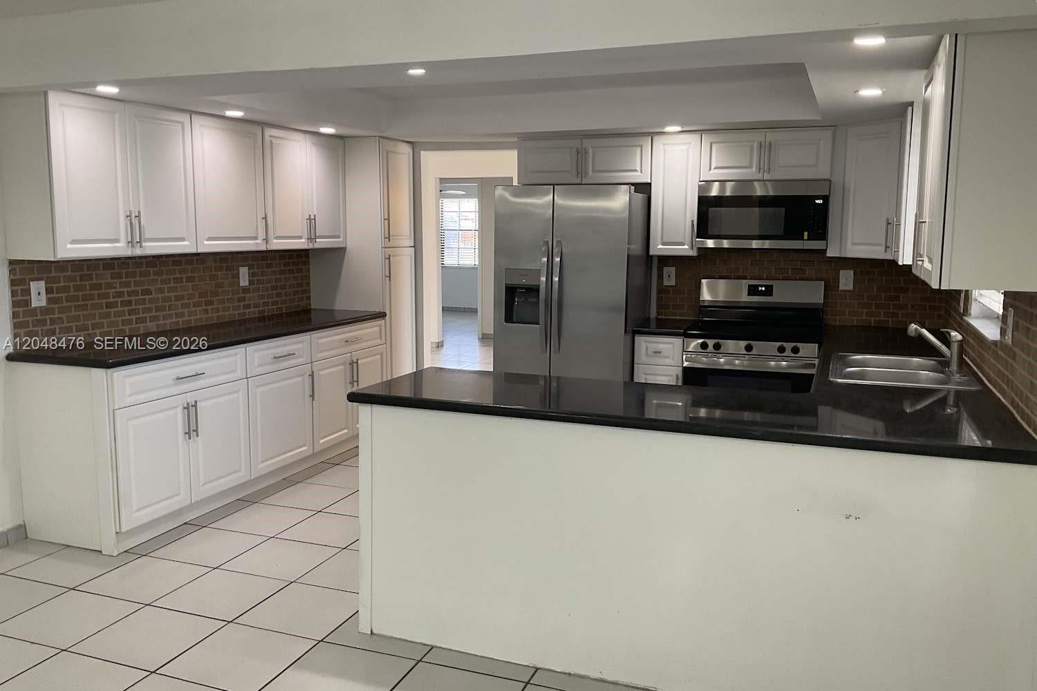 A kitchen features white cabinets, black countertops, stainless steel appliances, and a tiled backsplash — CUTLER BAY, FL