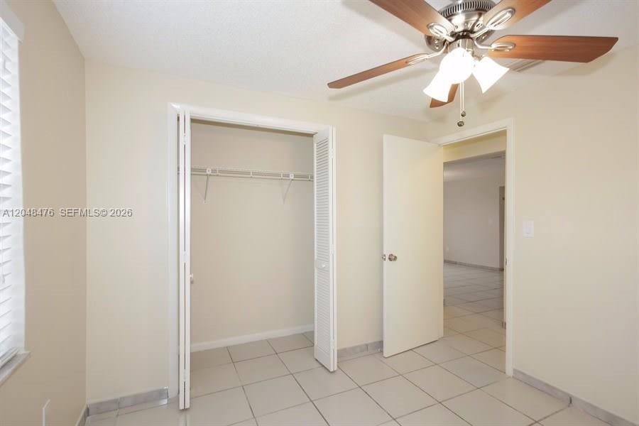 A bedroom features light-colored walls, tiled flooring, a ceiling fan, and an open closet — CUTLER BAY, FL