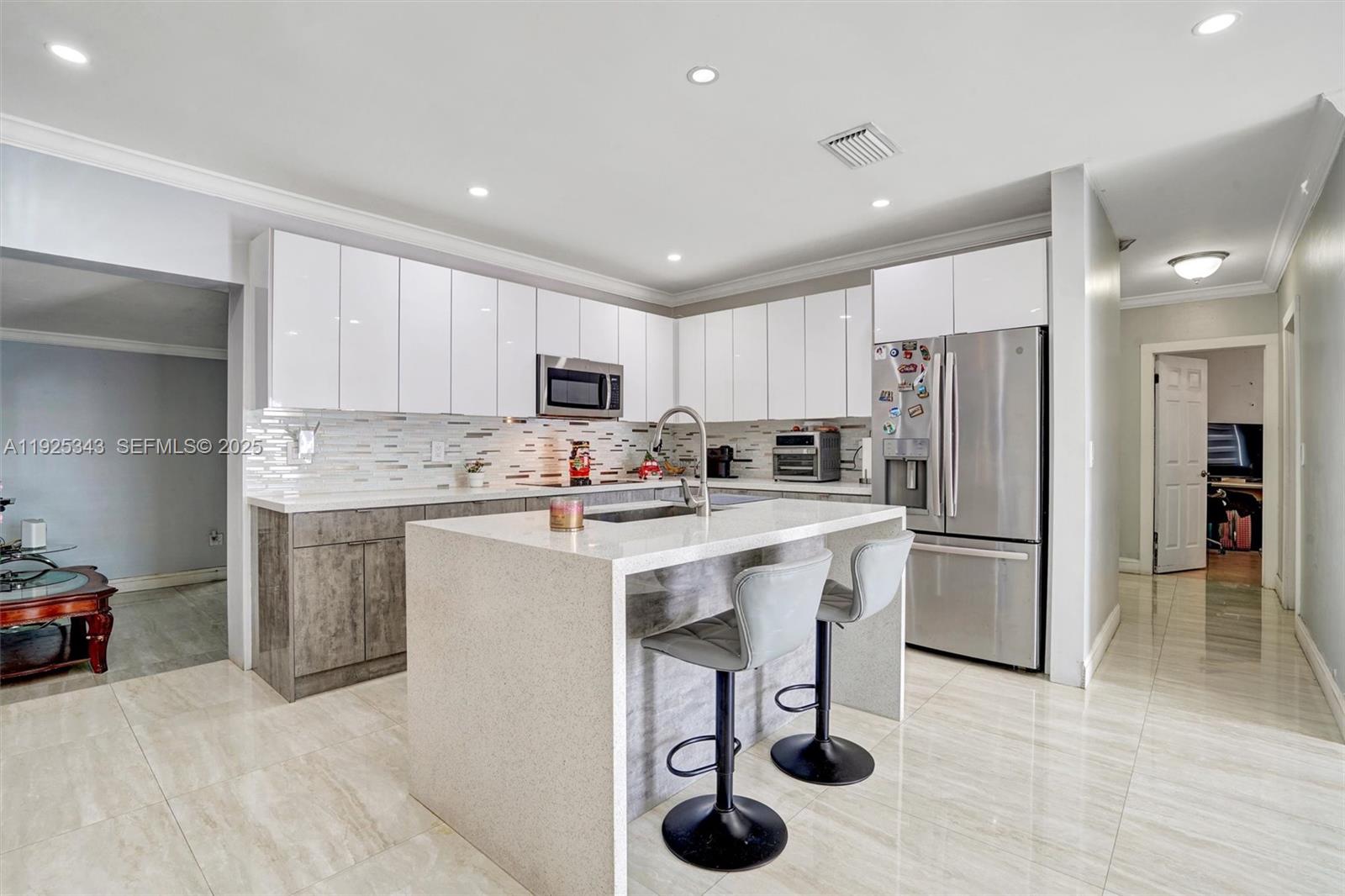 A modern open-concept living room and kitchen featuring light gray leather furniture and tile flooring — 631 E 53rd St, Hialeah FL 33013, HIALEAH, FL