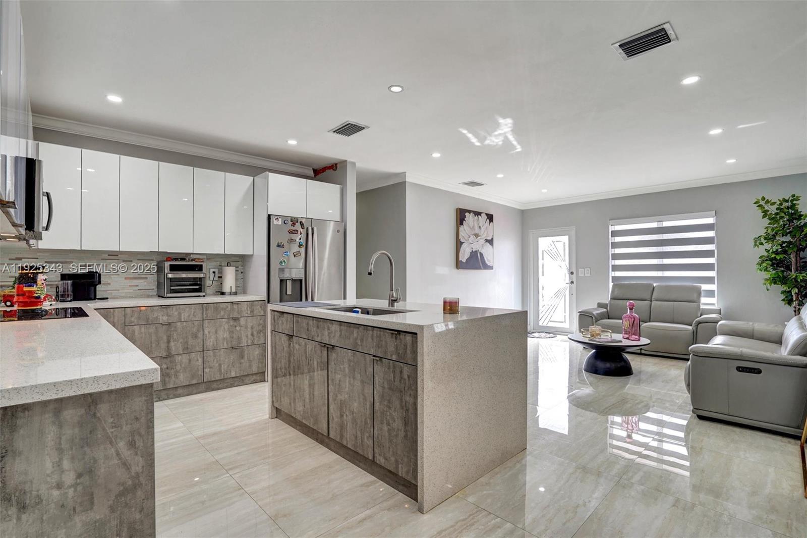A modern kitchen features white upper cabinets, gray lower cabinets, and a large quartz island — 631 E 53rd St, Hialeah FL 33013, HIALEAH, FL