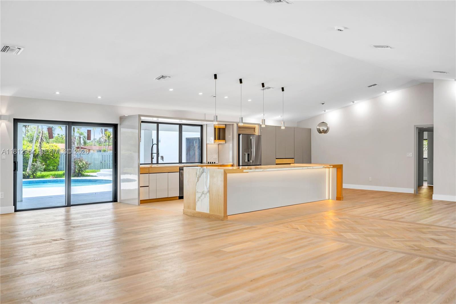 A modern kitchen features a large marble-topped island, light wood flooring, and sliding glass doors — 10600 SW 140th St, Miami FL 33176, MIAMI, FL