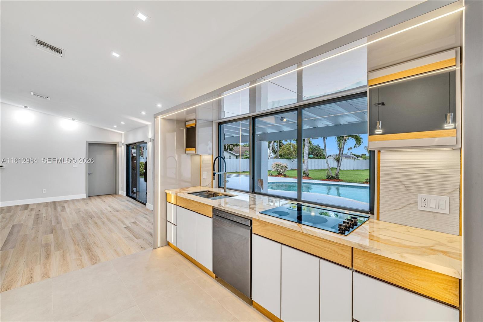 A modern kitchen features white cabinets, wood accents, a marble countertop, and a pool view — 10600 SW 140th St, Miami FL 33176, MIAMI, FL