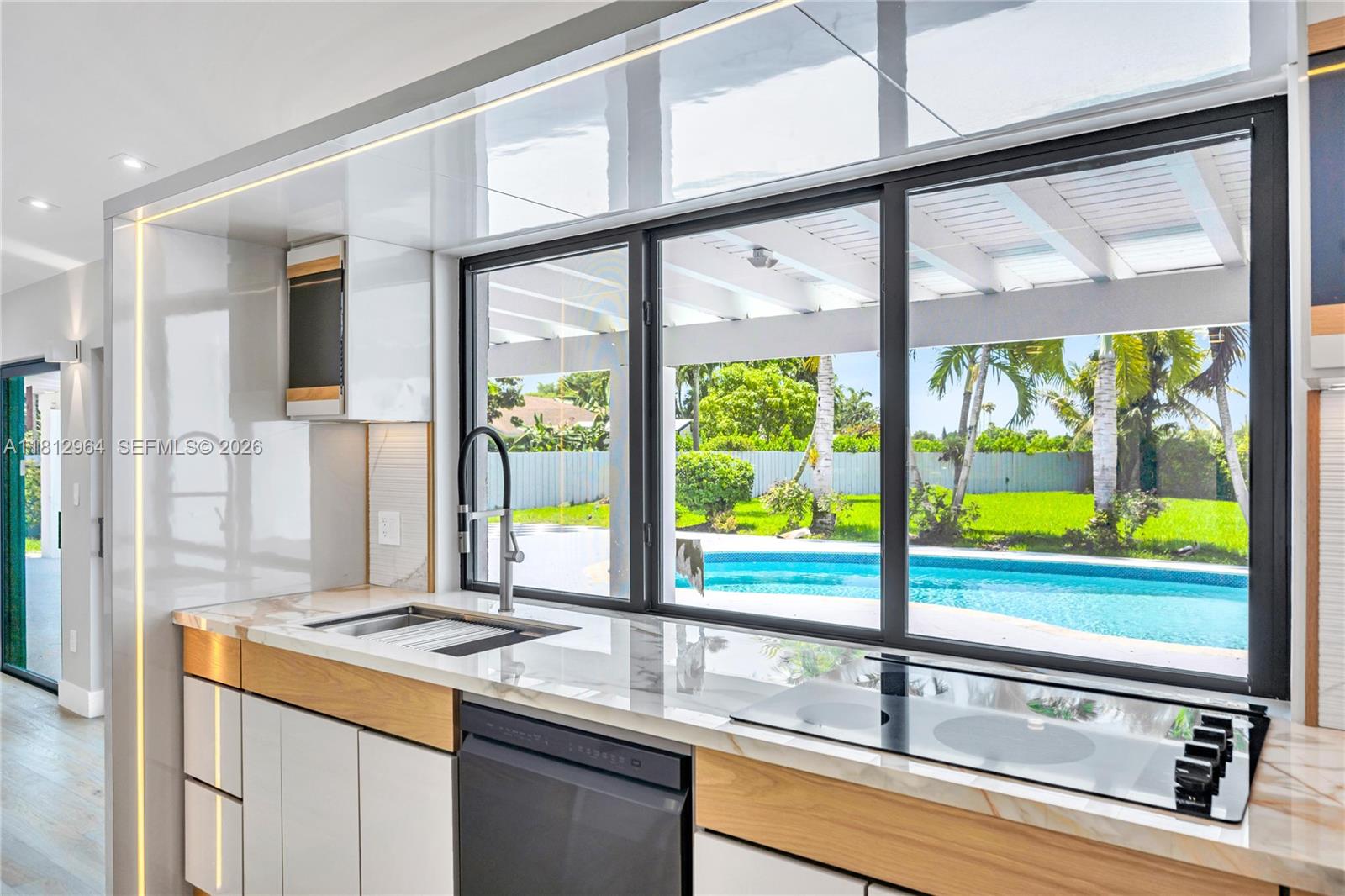 A modern kitchen features marble countertops, wood accents, and a large window overlooking a pool — 10600 SW 140th St, Miami FL 33176, MIAMI, FL