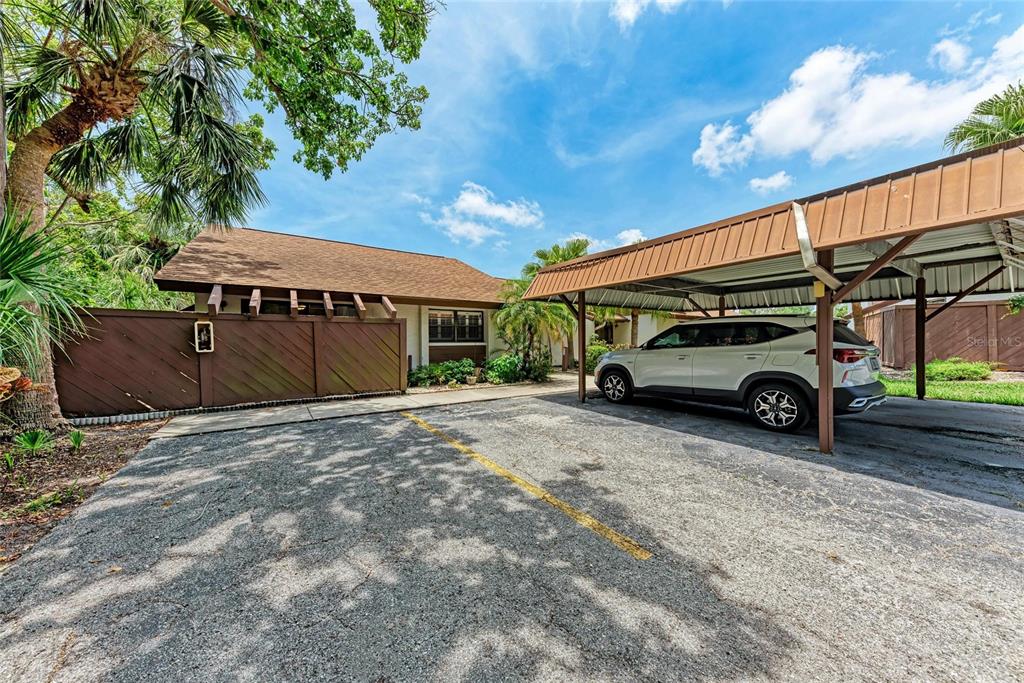 A white SUV is parked under a metal carport next to a house with a fence — 4644 RED MAPLE ROAD UNIT 1303, BRADENTON, FL