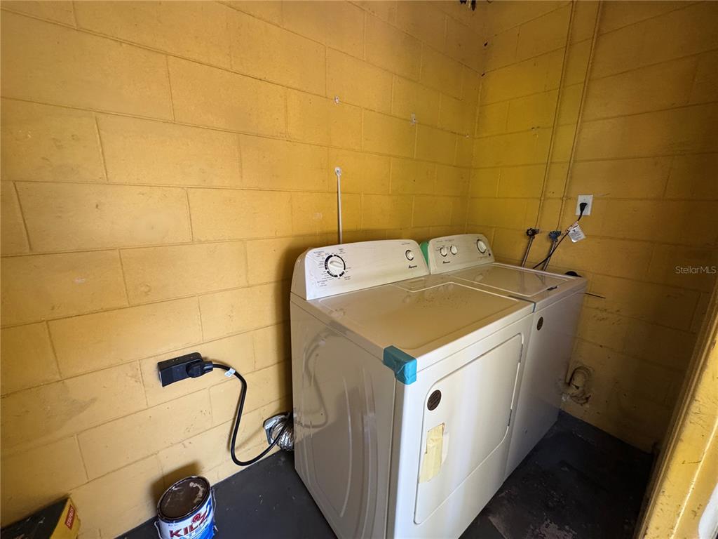 A laundry room features a white washer and dryer against a yellow concrete block wall — 2276 RAEFORD ROAD UNIT A4, ORLANDO, FL