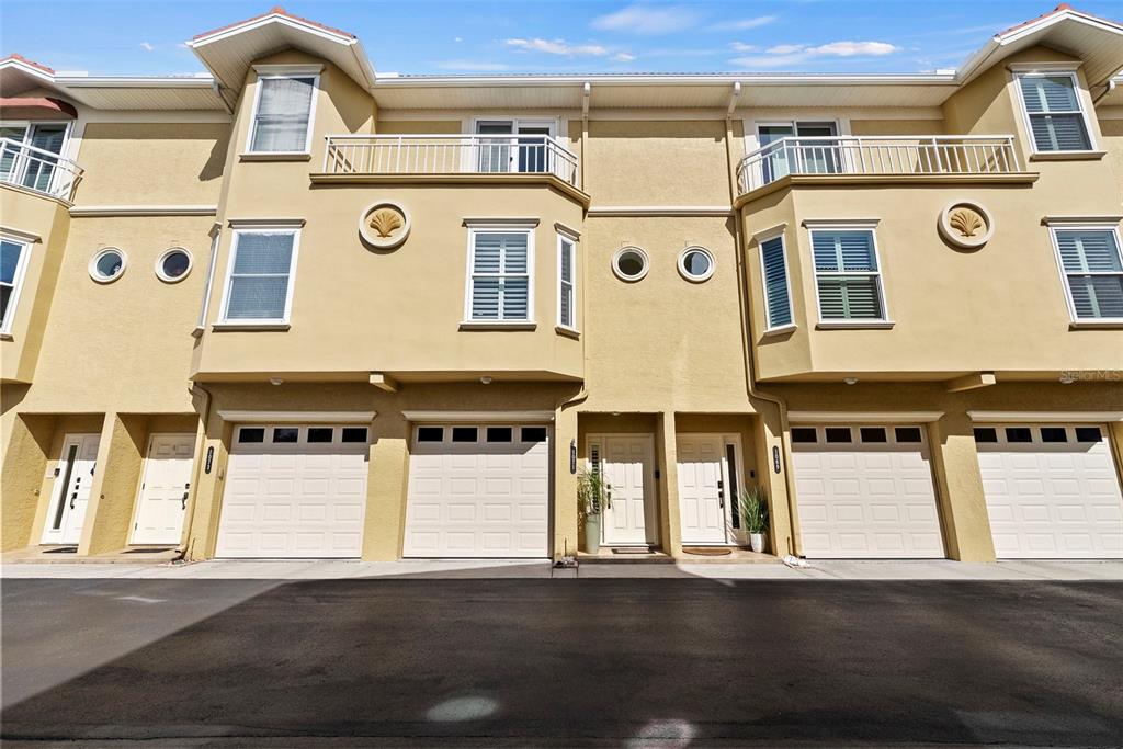 A row of beige townhouses featuring multiple garage doors, balconies, and circular accent windows — 1071 PINELLAS BAYWAY S, ST PETERSBURG, FL