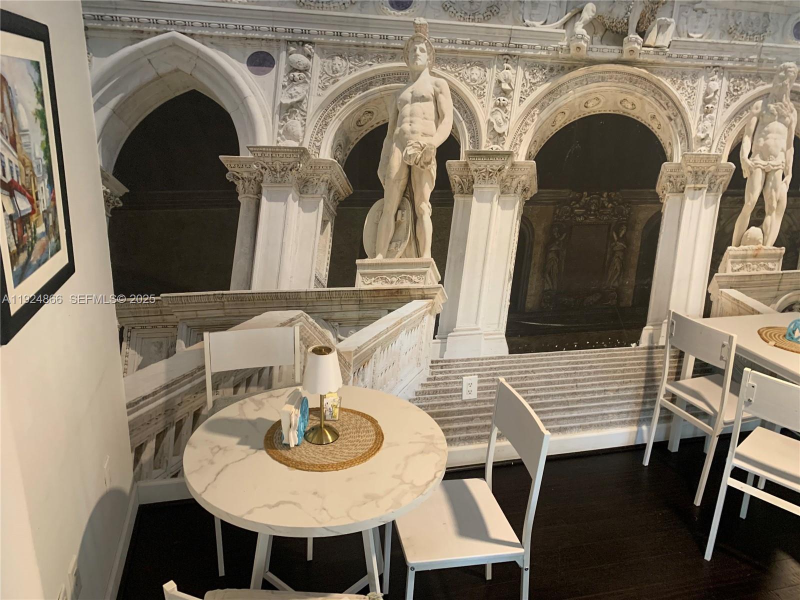 A dining area features a round marble table and white chairs against a mural wall — 1239 Alton Rd, Miami Beach FL 33139, MIAMI BEACH, FL