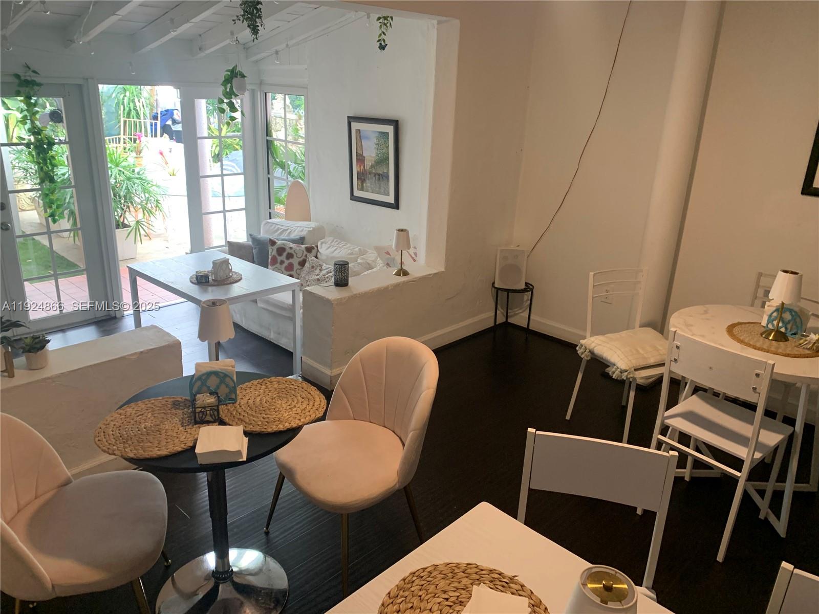 A dining area with multiple tables and chairs overlooks a sunlit patio through glass doors — 1239 Alton Rd, Miami Beach FL 33139, MIAMI BEACH, FL