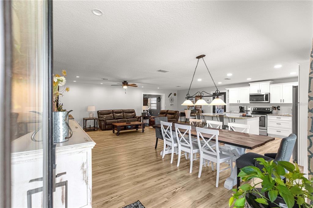 An open-concept living and dining area features light wood flooring and a white kitchen — 2940 NE 49TH STREET, OCALA, FL