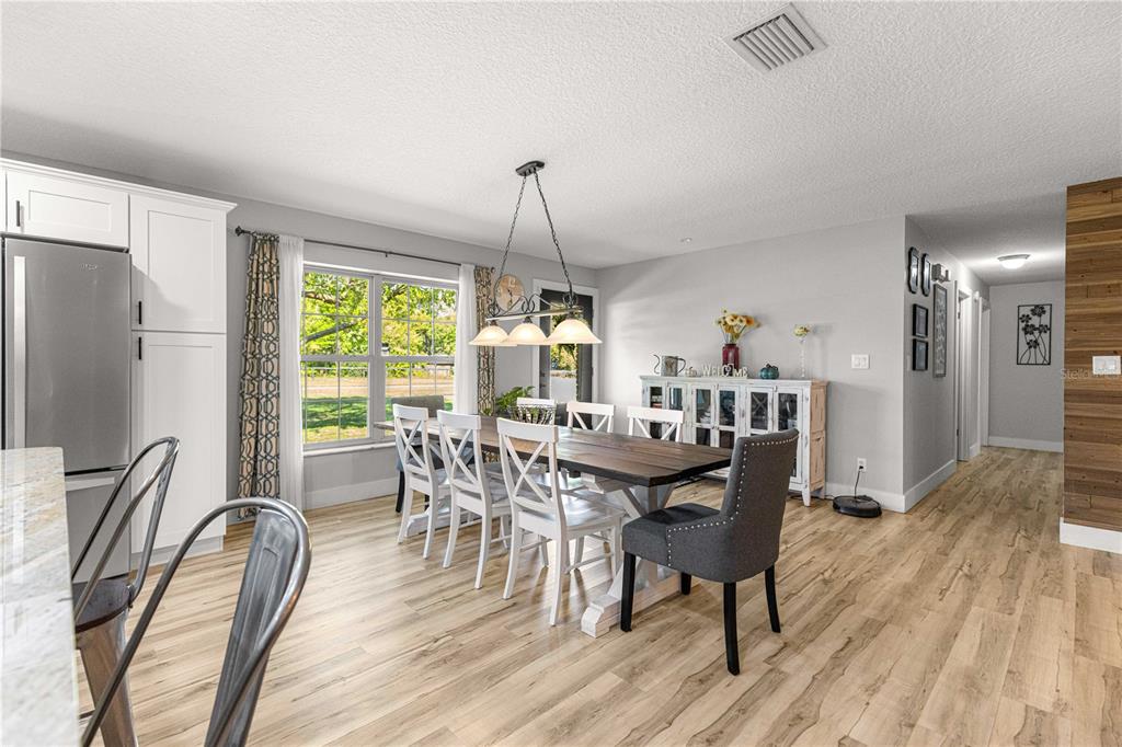 A dining room features a wooden table, white chairs, a gray upholstered chair, and wood-look flooring — 2940 NE 49TH STREET, OCALA, FL
