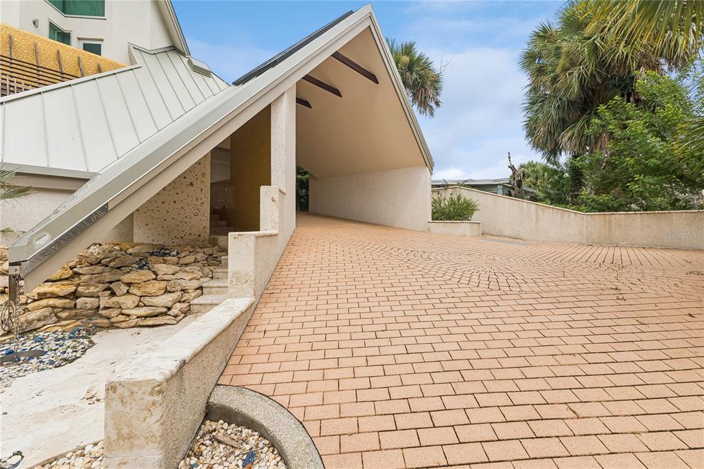 A paved driveway leads to a covered entryway with a modern, angular roofline and stone accents — 1800 N PENINSULA AVENUE, NEW SMYRNA BEACH, FL