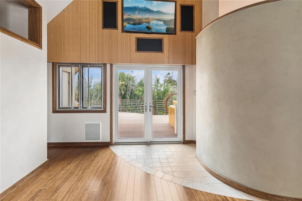 A room with wood flooring, a curved wall, and glass doors leading to a deck — 1800 N PENINSULA AVENUE, NEW SMYRNA BEACH, FL