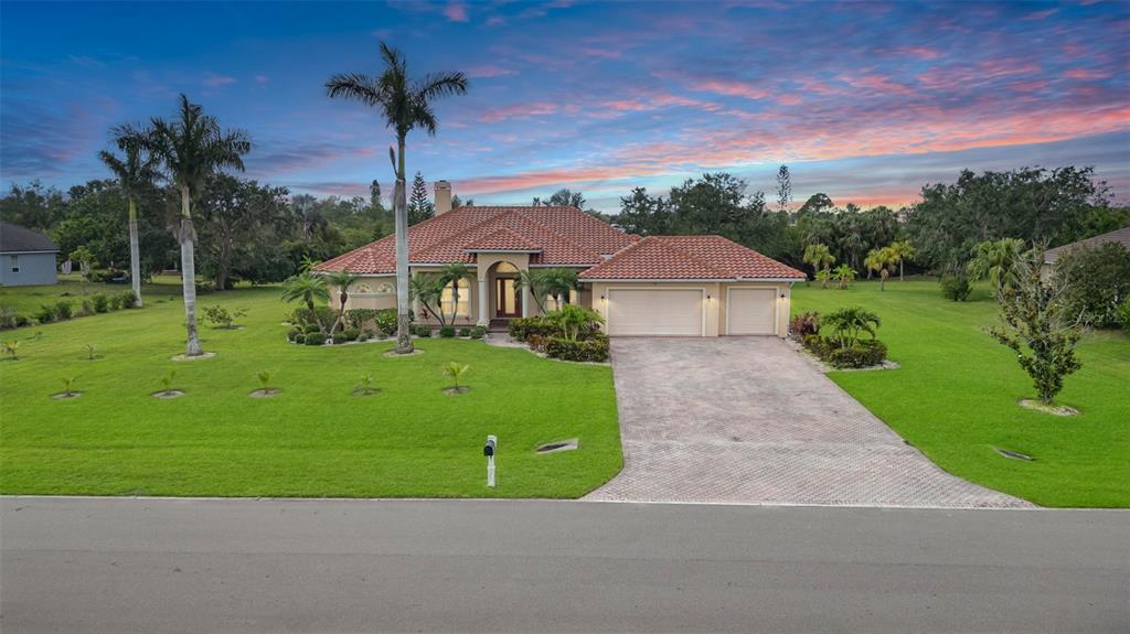 A single-story house with a tiled roof, three-car garage, and palm trees on a lawn — 6120 9TH AVENUE CIRCLE NE, BRADENTON, FL