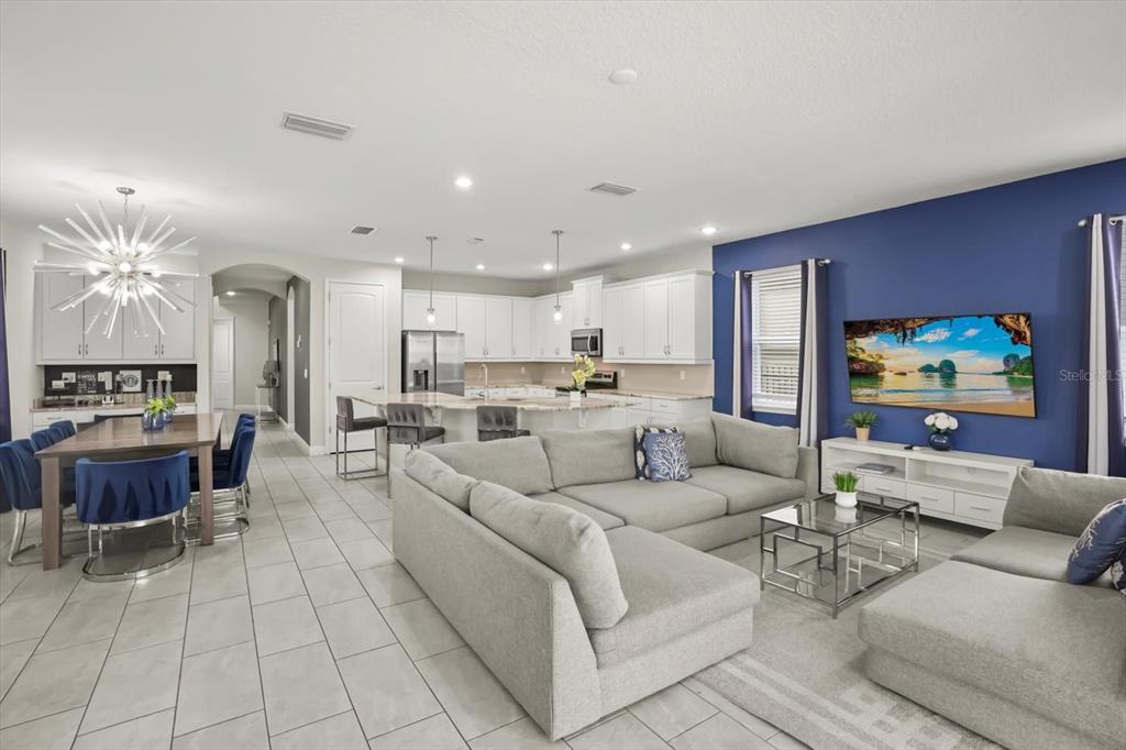 An open-concept living room and kitchen featuring a large sectional, dining area, and blue wall — 421 SOUTHFIELD STREET, KISSIMMEE, FL