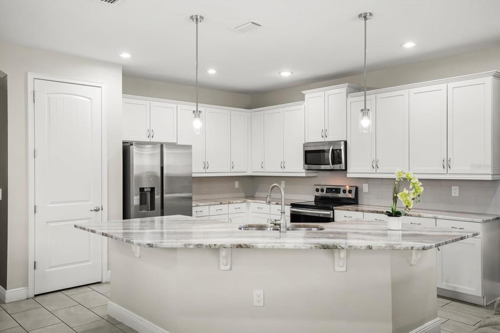 A modern kitchen features white cabinetry, stainless steel appliances, and a large stone-topped island — 421 SOUTHFIELD STREET, KISSIMMEE, FL