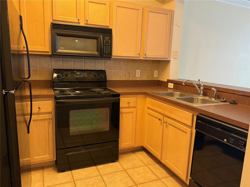A kitchen features light wood cabinets, black appliances, a tiled backsplash, and laminate countertops — 12861 MADISON POINTE CIRCLE UNIT 106, ORLANDO, FL