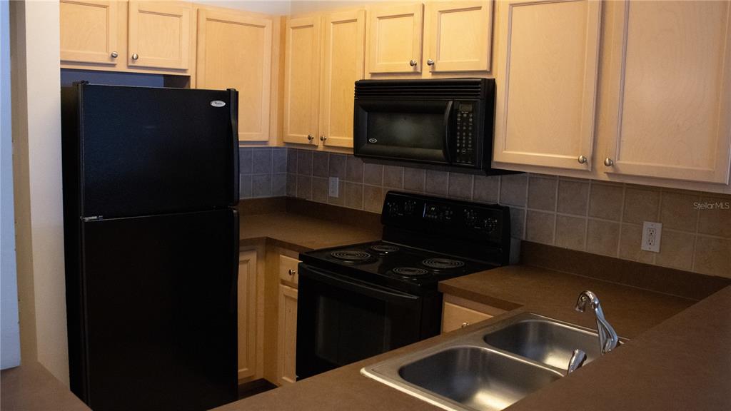 A kitchen features light wood cabinets, black appliances, brown countertops, and a double-basin sink — 12861 MADISON POINTE CIRCLE UNIT 106, ORLANDO, FL