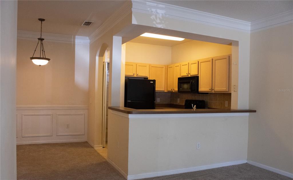 A kitchen with light wood cabinets and black appliances overlooks a carpeted living area — 12861 MADISON POINTE CIRCLE UNIT 106, ORLANDO, FL