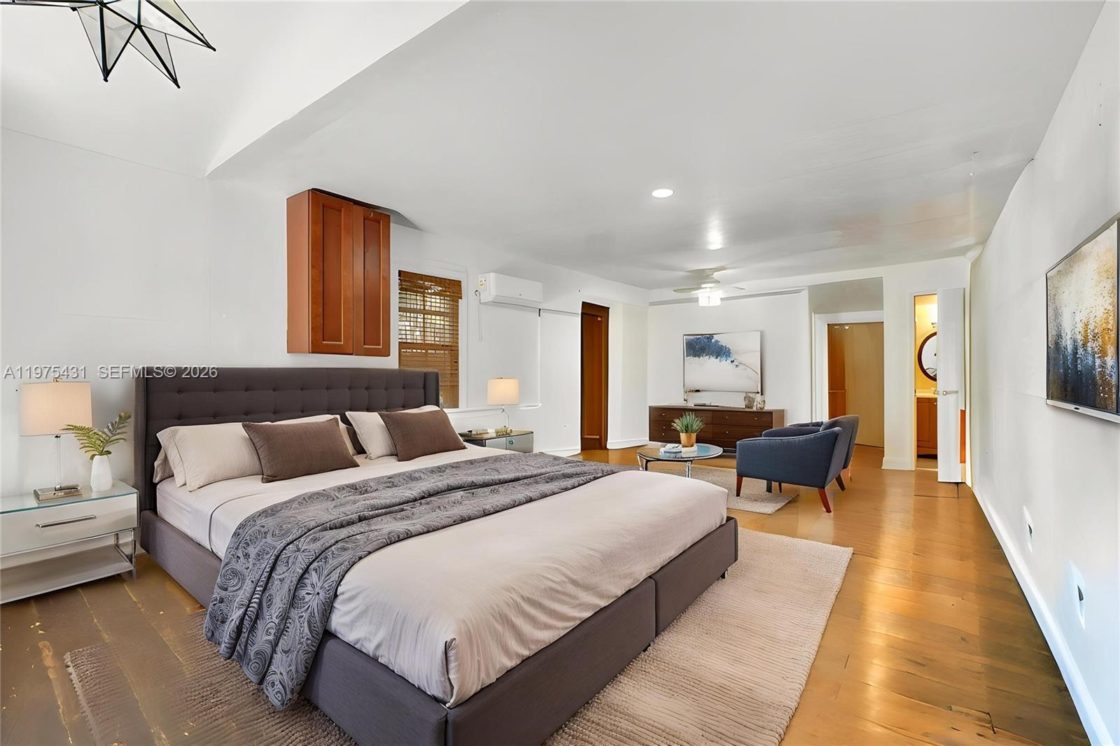 A spacious bedroom features a grey upholstered bed, hardwood floors, and a seating area — 11809 NE 1st Ave, Miami FL 33161, MIAMI, FL