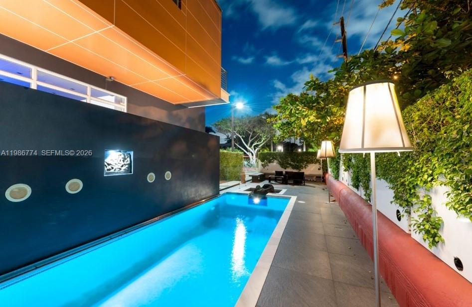 A rectangular swimming pool sits beside a modern building with a dark wall and lighting — 1606 S Bayshore Dr, Miami FL 33133, MIAMI, FL