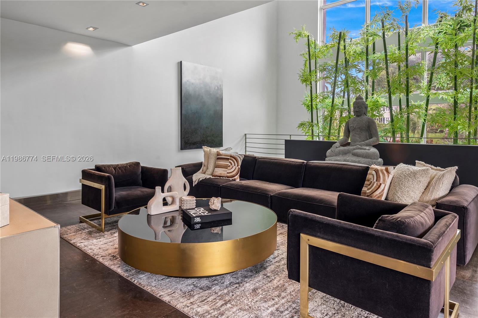 A modern living room features a dark sectional, gold-accented chairs, and a large Buddha statue — 1606 S Bayshore Dr, Miami FL 33133, MIAMI, FL