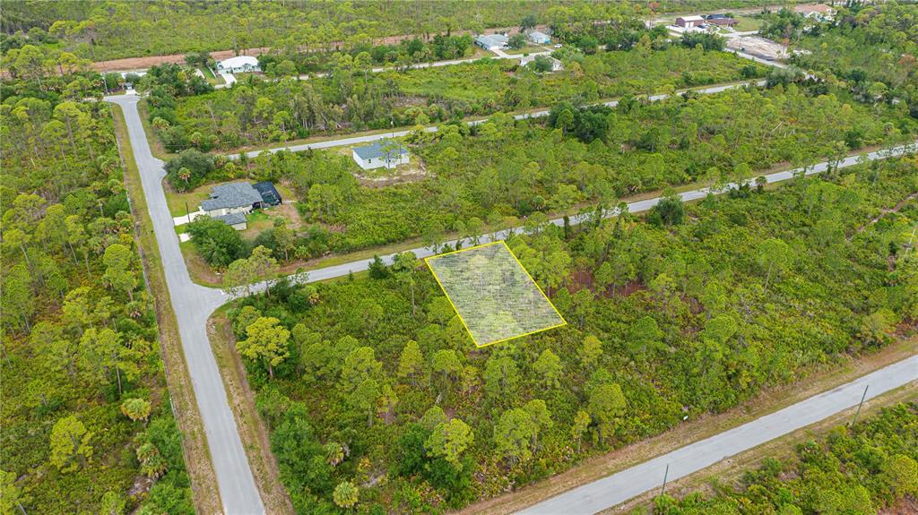 An aerial view shows a vacant, rectangular lot outlined in yellow amidst wooded residential land — 474 HANSCOM STREET, PORT CHARLOTTE, FL