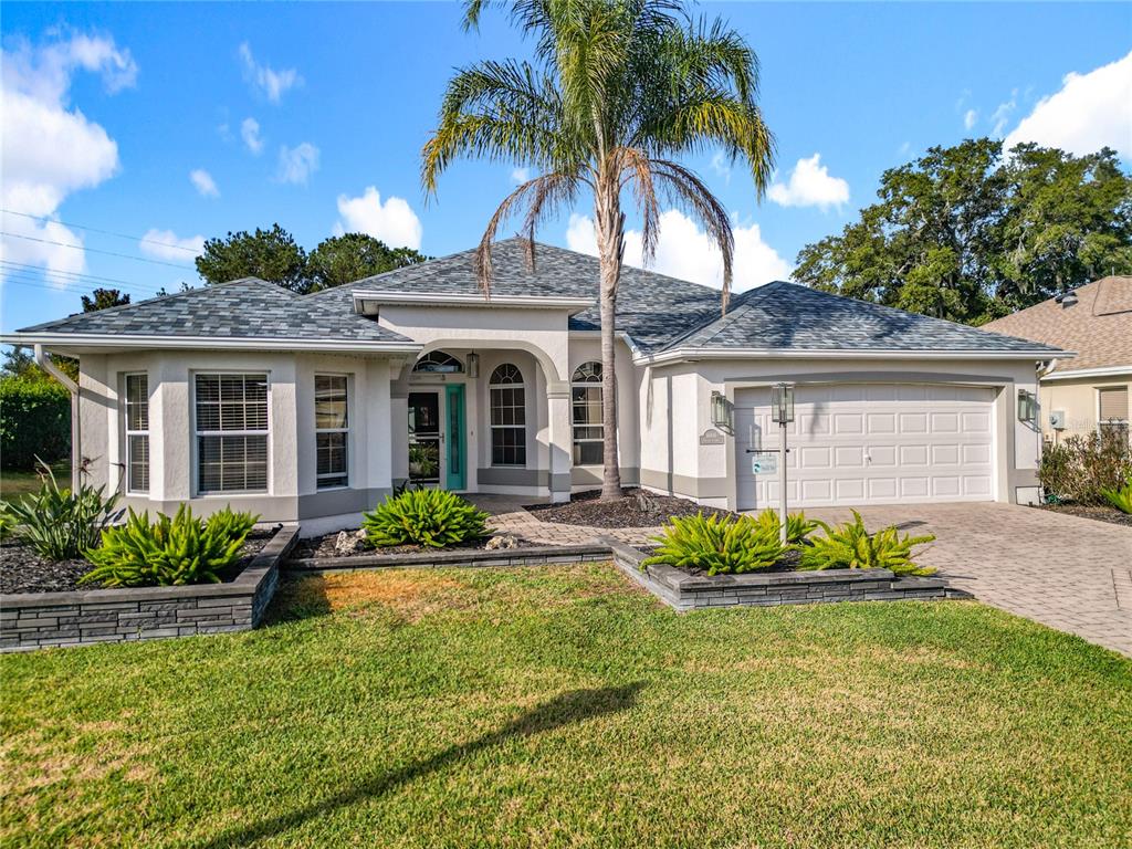 A single-story house with a white stucco exterior, a palm tree, and a paved driveway — 16816 SE 85TH SAPELO COURT, THE VILLAGES, FL