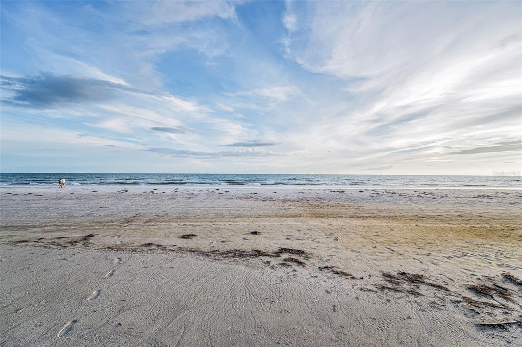A wide, sandy beach meets the ocean under a vast, cloudy blue sky — 16200 GULF BOULEVARD, REDINGTON BEACH, FL