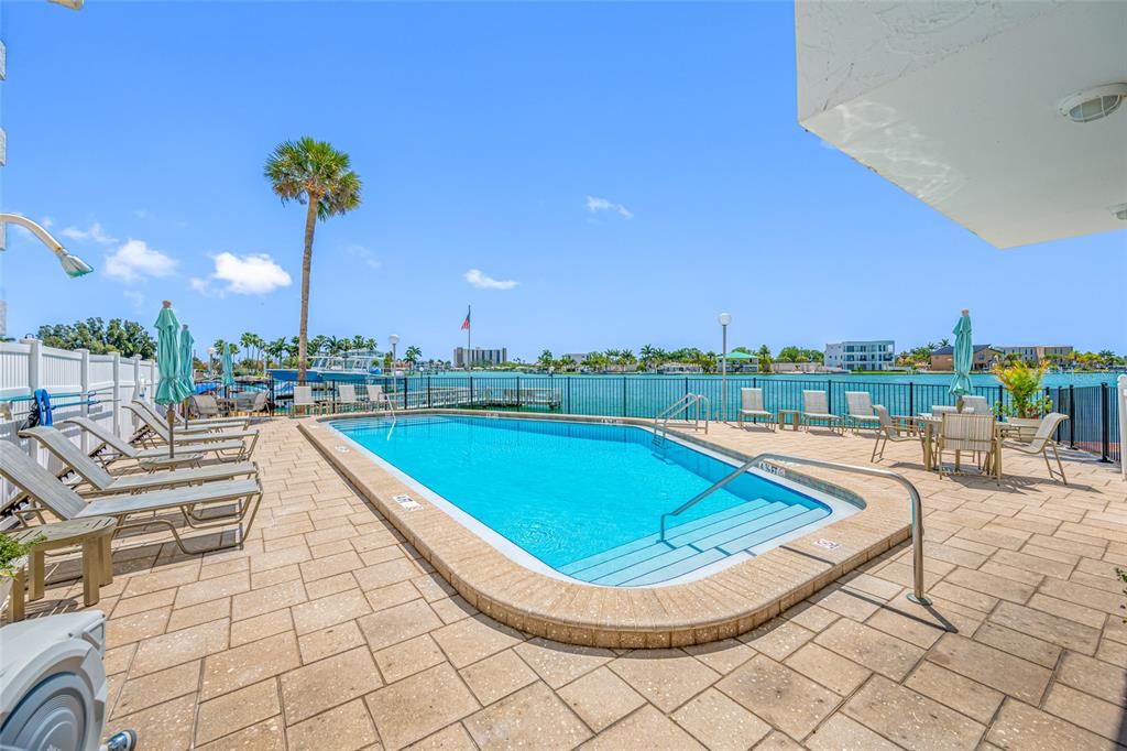 A swimming pool with lounge chairs on a paved deck overlooking a bay — 285 107TH AVENUE UNIT 306, TREASURE ISLAND, FL