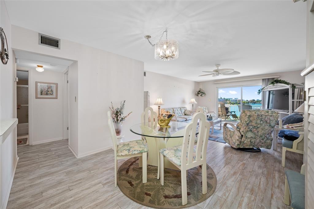 A dining area with a glass table and chairs opens into a living room overlooking water — 285 107TH AVENUE UNIT 306, TREASURE ISLAND, FL
