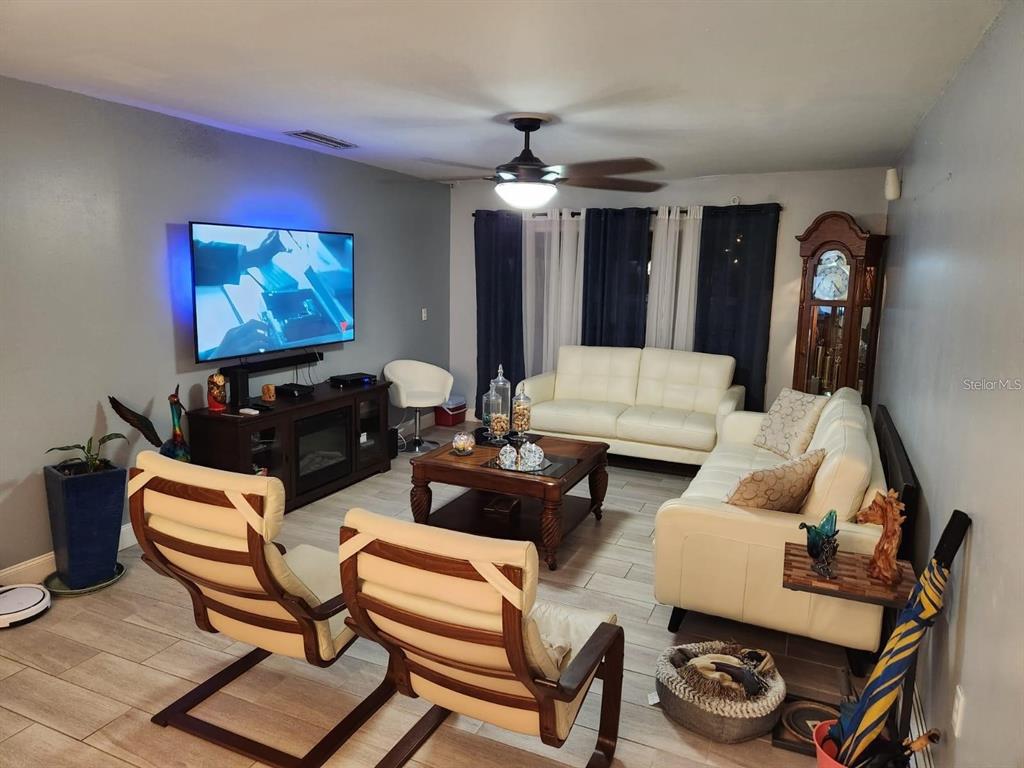 A living room features white leather sofas, wood-framed chairs, a coffee table, and a television — 3801 S LAKE DRIVE UNIT 247, TAMPA, FL