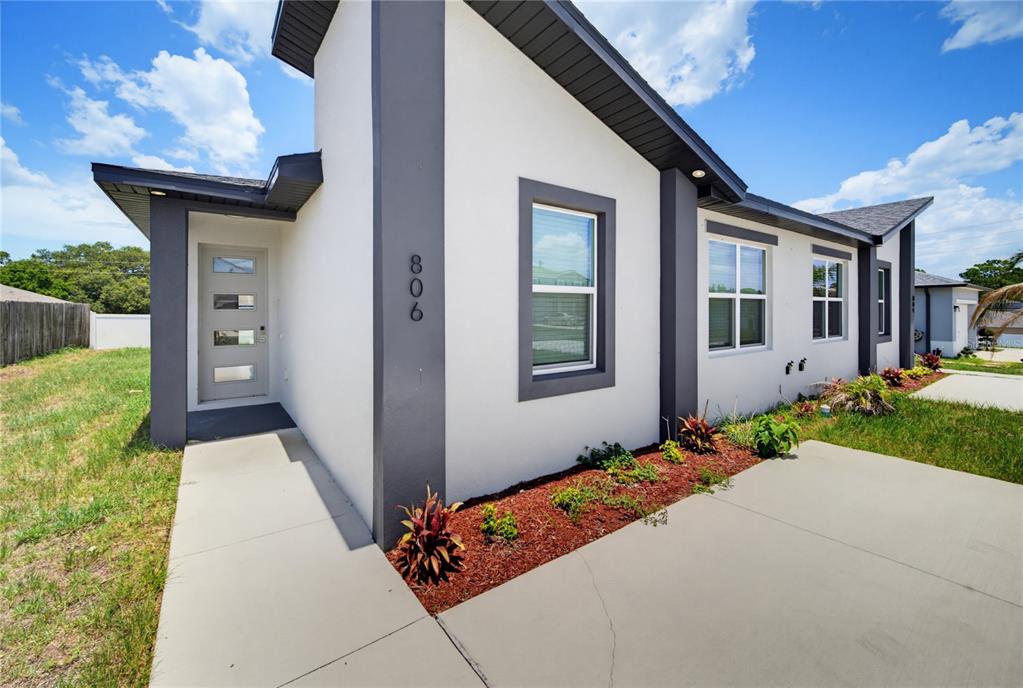 A modern house exterior features white stucco walls, dark gray trim, and a concrete walkway — 806 COLVILLE DRIVE, KISSIMMEE, FL