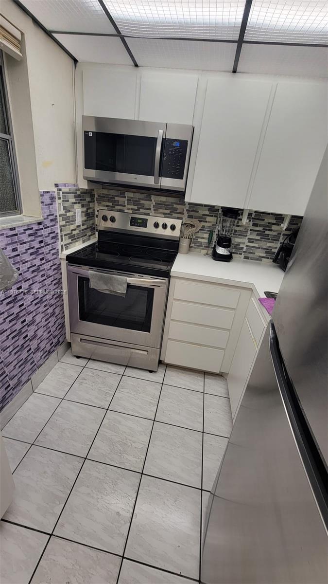 A small kitchen features white cabinets, stainless steel appliances, and purple tiled walls — 6820 W Flagler St # 207, Miami FL 33144, MIAMI, FL