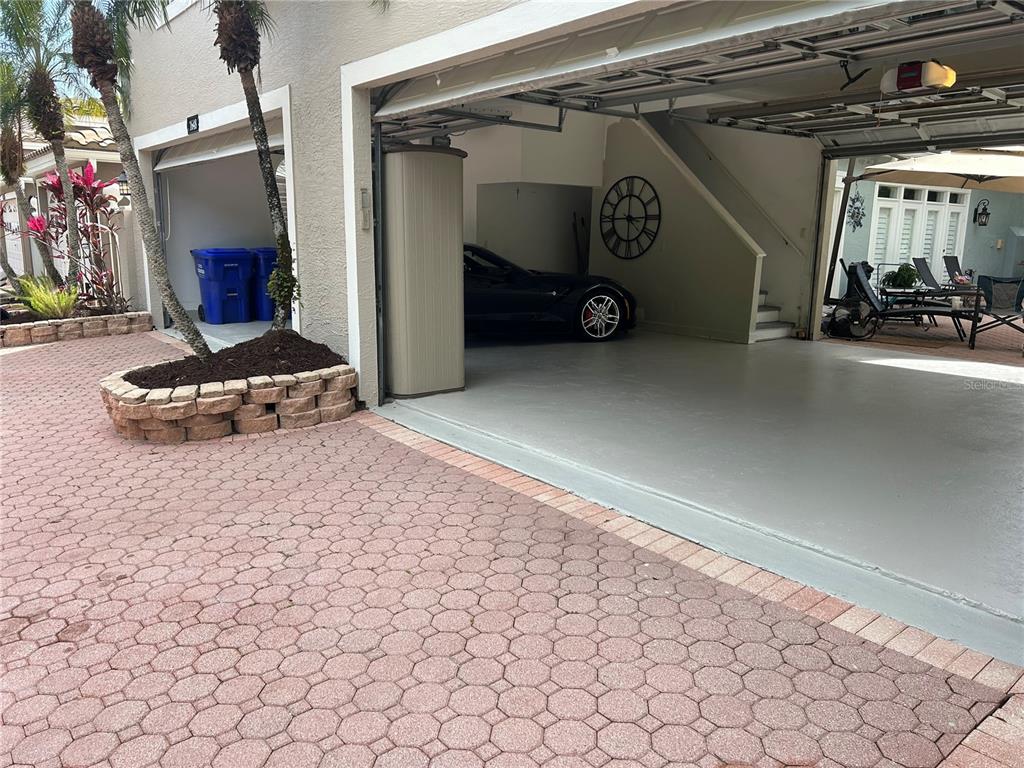 A two-car garage with a gray epoxy floor, a parked sports car, and a large wall clock — 1648 LAGO VISTA BOULEVARD, PALM HARBOR, FL