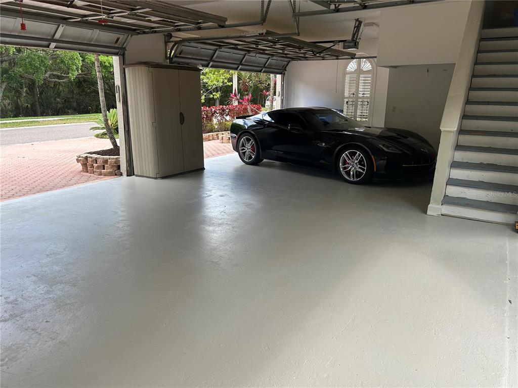 A spacious garage with a light-colored floor, a black sports car, and an interior staircase — 1648 LAGO VISTA BOULEVARD, PALM HARBOR, FL